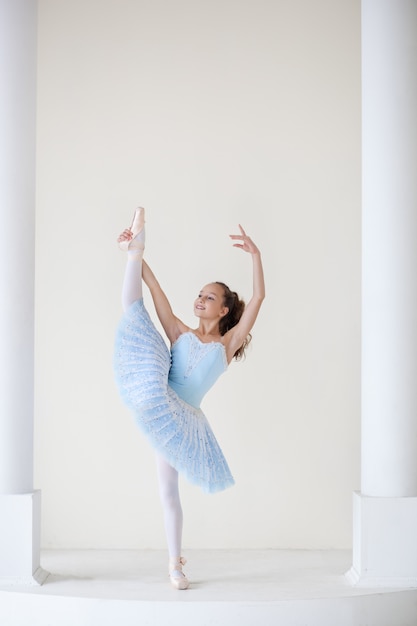 Una ballerina carina in costume da balletto e in punta sta ballando in uno studio bianco. Ragazza nella classe di danza. La ragazza studia balletto. La ballerina sta ballando. Bellissima ballerina che si esercita allo specchio.