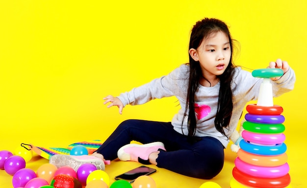 Una bambina abbastanza asiatica si diverte a fare pratica per inserire un cerchio di plastica colorato nel cono triangolare per conoscere la sequenza delle dimensioni, la pila di strati e la forma mentre è seduto sul bambino che gioca sul pavimento di una palla divertente e un giocattolo