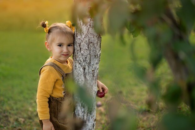 Una bambina abbraccia un tronco d'albero in una calda serata autunnale al tramonto