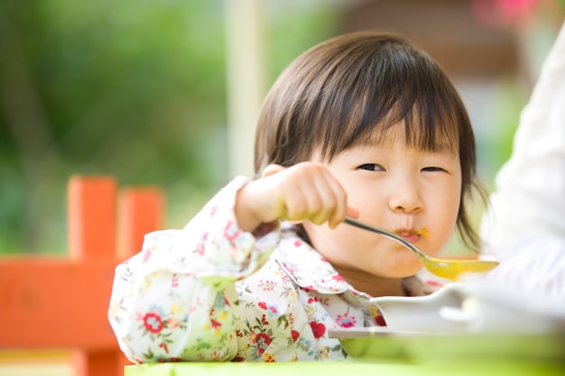 È una bambina adorabile seduta accanto a sua madre e che mangia minestra.