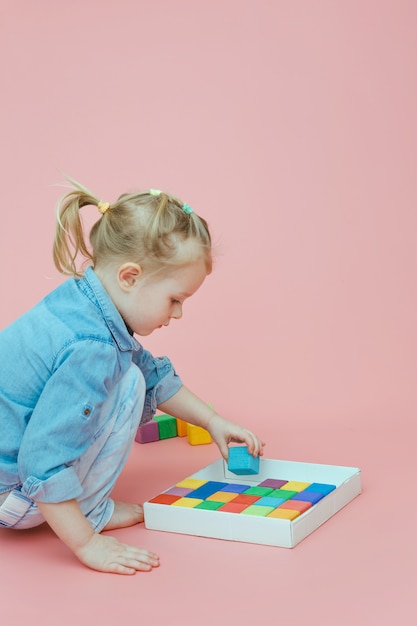 Una bambina affascinante in abiti in denim su uno sfondo rosa