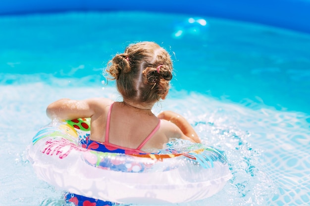 Una bambina affascinante in un costume da bagno luminoso impara a nuotare nella piscina nel giardino