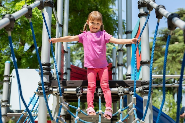 Una bambina allegra cammina su un ponte di corda in un parco giochi nel parco