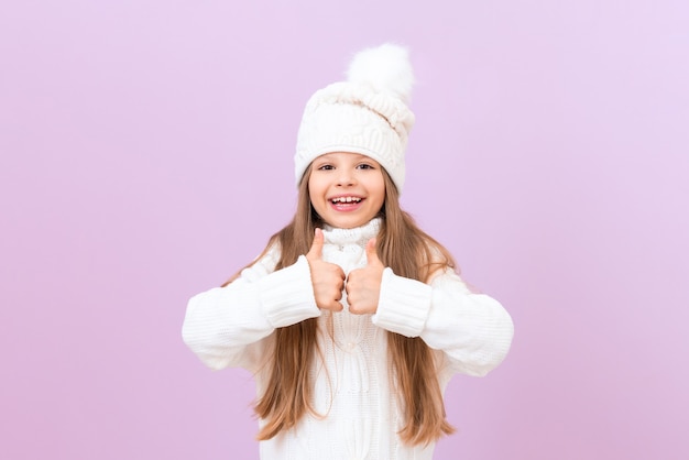 Una bambina allegra con un cappello caldo d'inverno mostra i suoi pollici in su.