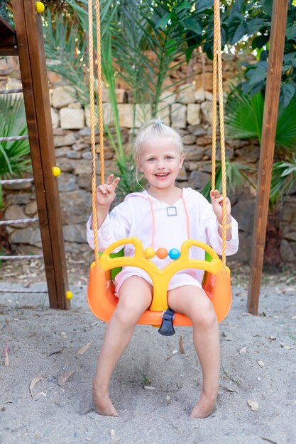 Una bambina allegra e gioiosa oscilla su un'altalena su una piattaforma di legno in estate e sorride