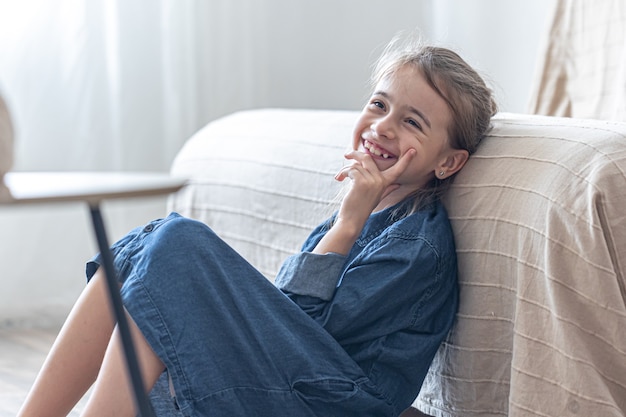 Una bambina allegra è seduta, appoggiata al divano.