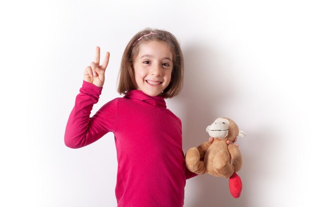 Una bambina allegra mostra un segno di vittoria mentre tiene in mano un peluche scimmia