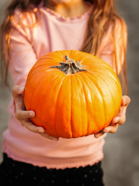 Una bambina allegra tiene una zucca arancione nel parco in autunno. Oggetti di scena di Halloween