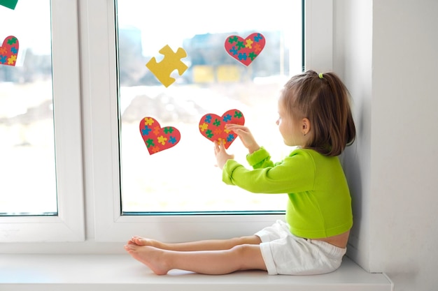 Una bambina appende cartoline a forma di cuori e puzzle sul vetro