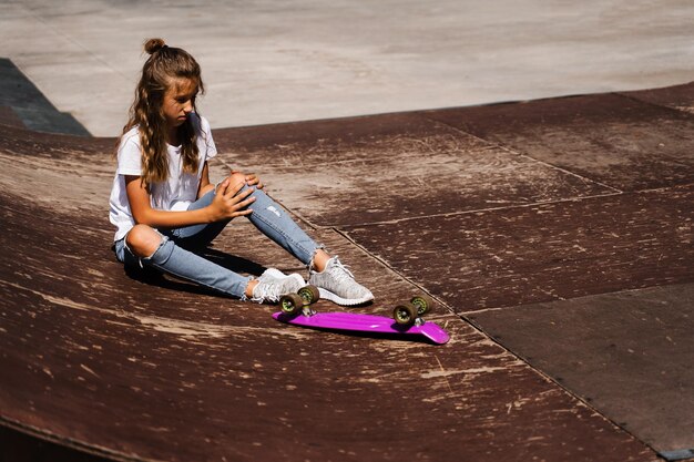 Una bambina attiva dopo la caduta da un penny board si è infortunata seduta e sente dolore sulla rampa sportiva nel parco giochi dello skate park