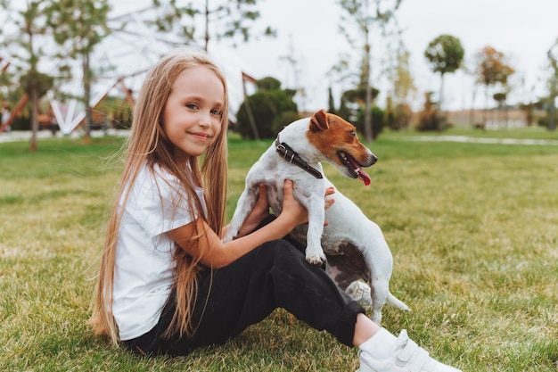Una bambina bacia e abbraccia il suo cane Jack Russell terrier nel parco L'amore tra il proprietario e il cane un bambino tiene in braccio un cane