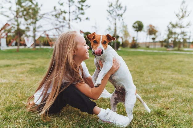 Una bambina bacia e abbraccia il suo cane Jack Russell terrier nel parco L'amore tra il proprietario e il cane un bambino tiene in braccio un cane