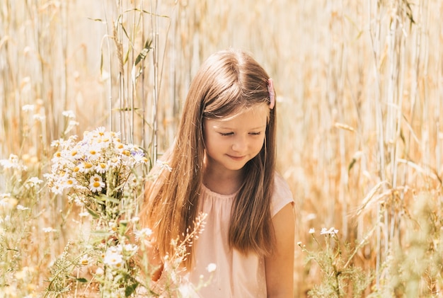 Una bambina bellissima con un mazzo di margherite in un campo di grano