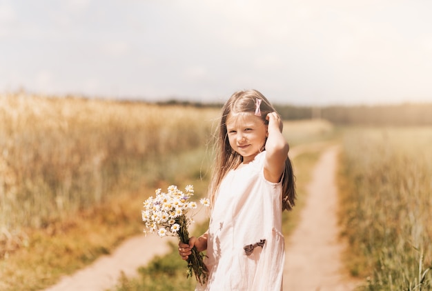 Una bambina bellissima con un mazzo di margherite in un campo di grano