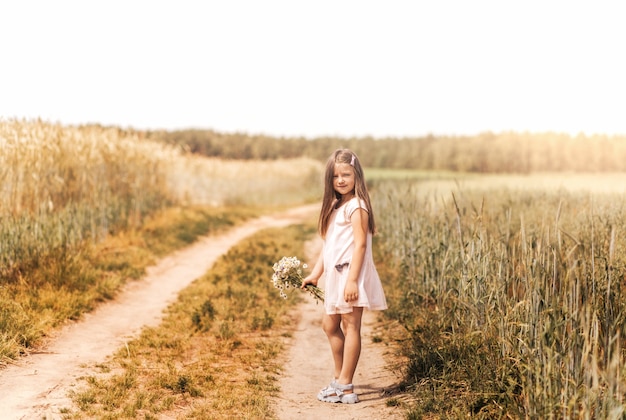 Una bambina bellissima con un mazzo di margherite in un campo di grano