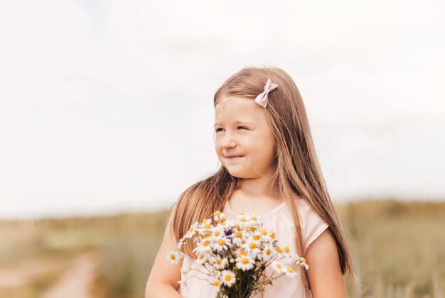 Una bambina bellissima con un mazzo di margherite in un campo di grano