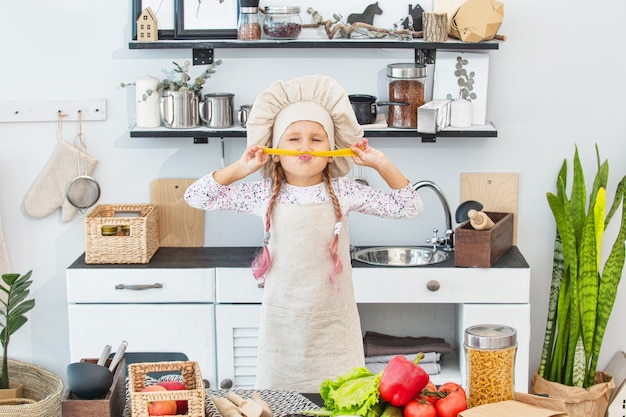 Una bambina bellissima cuoca in cucina con diverse verdure e spaghetti