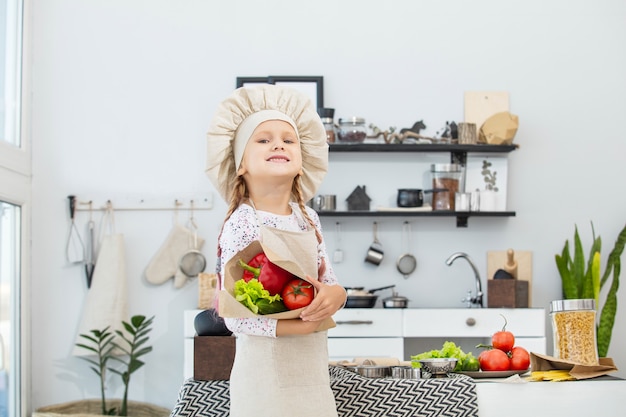 Una bambina bellissima cuoca in cucina con diverse verdure e spaghetti