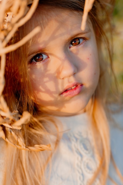 Una bambina bionda con un cappello di paglia in estate al tramonto