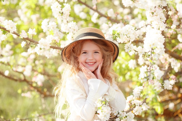 Una bambina bionda con un cappello di paglia vicino a un albero in fiore