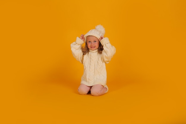 una bambina bionda con un maglione bianco lavorato a maglia un cappello bianco e calzini lavorati a maglia