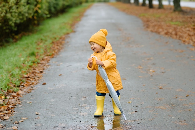 Una bambina cammina con un ombrello in stivali di gomma gialli e un impermeabile impermeabile. Passeggiata autunnale