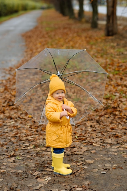 Una bambina cammina con un ombrello in stivali di gomma gialli e un impermeabile impermeabile. Passeggiata autunnale