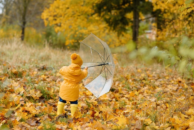 Una bambina cammina con un ombrello in stivali di gomma gialli e un impermeabile impermeabile. Passeggiata autunnale