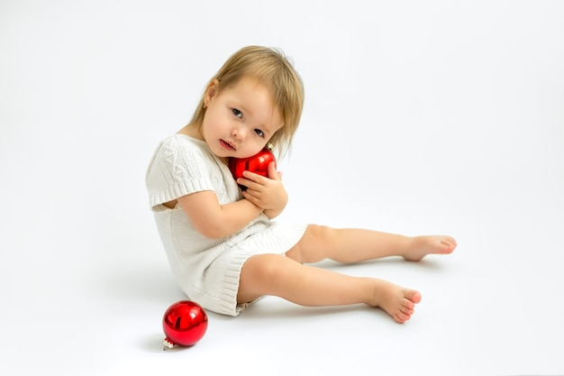 Una bambina carina abbraccia una palla di Natale di vetro rosso