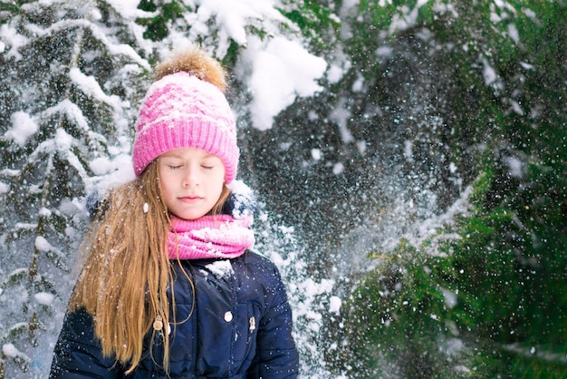 Una bambina carina con gli occhi chiusi e gli abeti innevati dietro