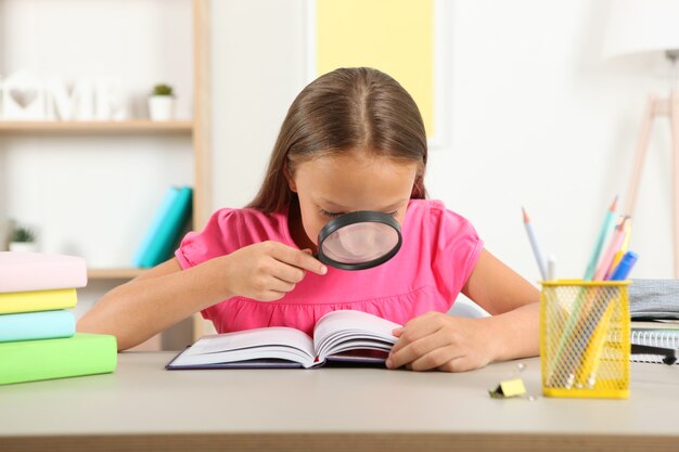 Una bambina carina con problemi di vista legge con una lente d'ingrandimento