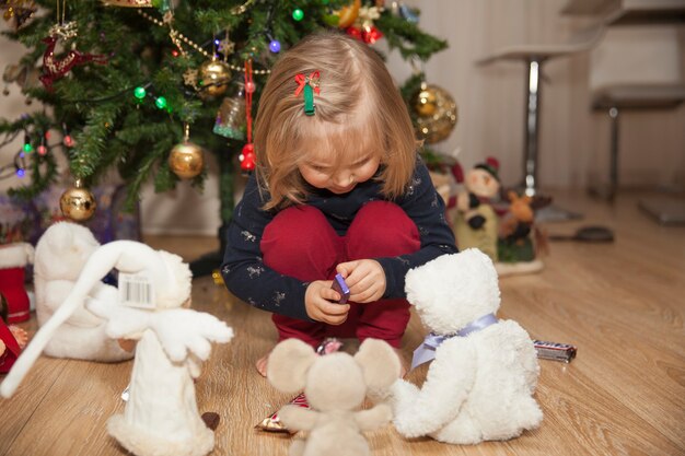 Una bambina carina con regali di Natale seduta vicino all'albero di Natale nella stanza, concetto di Capodanno