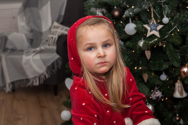 Una bambina carina con regali di Natale seduta vicino all'albero nella stanza, concetto di Capodanno