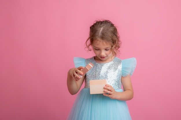 Una bambina carina con un bel vestito tiene la bacchetta magica di una fata e un regalo su uno sfondo rosa