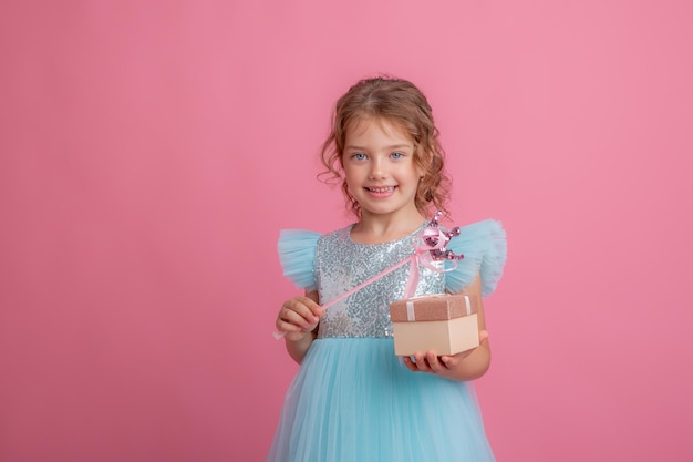 Una bambina carina con un bel vestito tiene la bacchetta magica di una fata e un regalo su uno sfondo rosa