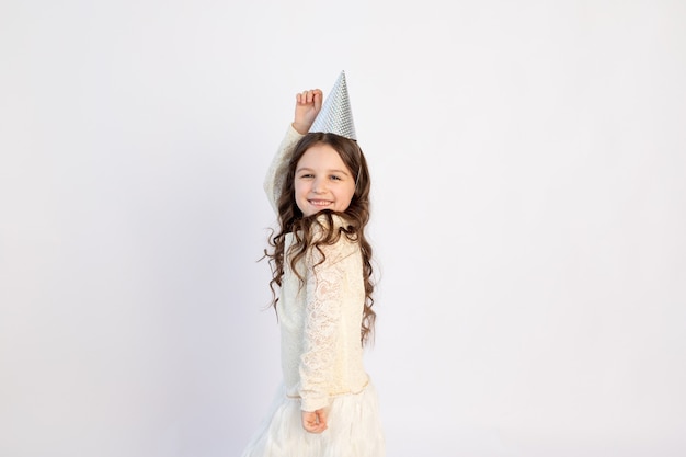Una bambina carina con un berretto su uno sfondo bianco isolato sta ballando e gioendo. Spazio per il testo