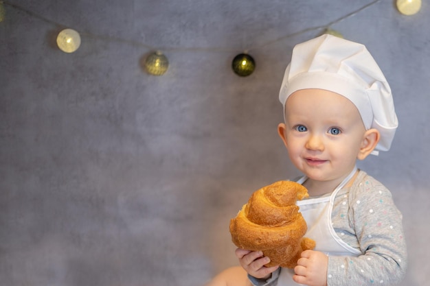Una bambina carina con un cappello da chef e un grembiule si siede a casa sul tavolo in cucina