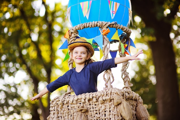 Una bambina carina con un cappello di paglia sorride in un cesto di palloncini. Infanzia, avventura