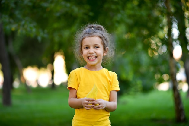 Una bambina carina con una maglietta gialla sullo sfondo di alberi verdi