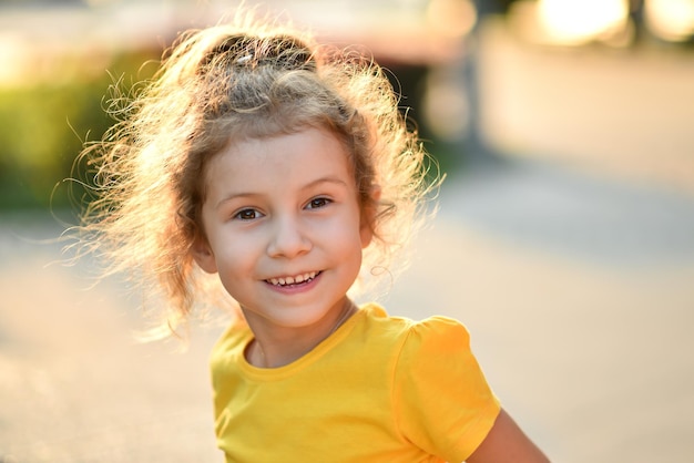 Una bambina carina con una maglietta gialla sullo sfondo di alberi verdi.
