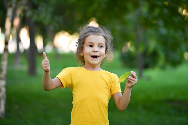 Una bambina carina con una maglietta gialla sullo sfondo di alberi verdi