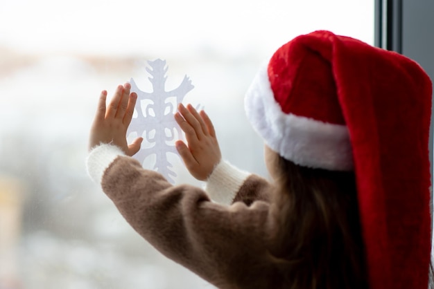 Una bambina carina decora le finestre con fiocchi di neve Capodanno Natale Atmosfera