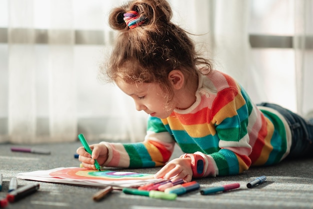 Una bambina carina disegna un arcobaleno con pennarelli colorati Creation Childhood