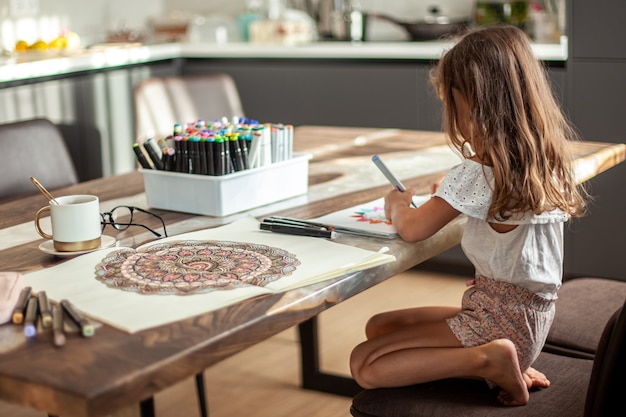 Una bambina carina disegna un motivo circolare di mandala nell'album con pennarelli artistici