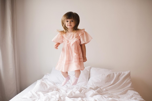 Una bambina carina e divertente che indossa un vestito rosa alla moda salta a letto