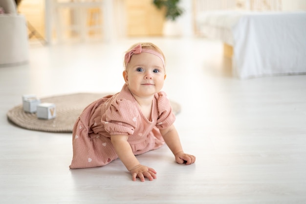 Una bambina carina e sana fino a un anno con un vestito rosa in tessuto naturale è seduta su un tappeto nel soggiorno di casa giocando con cubi di legno lo sviluppo del bambino a casa
