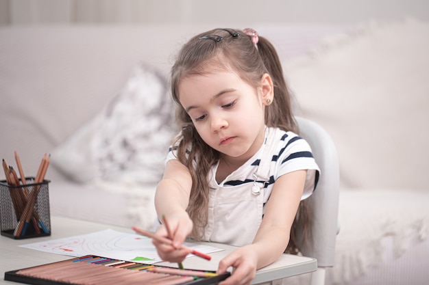 Una bambina carina è seduta al tavolo e fa i compiti. Homeschooling e concetto di istruzione.