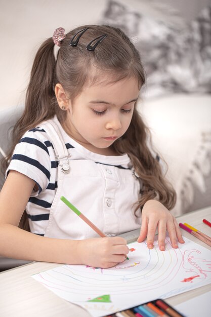 Una bambina carina è seduta al tavolo e sta facendo i compiti. Homeschooling e concetto di istruzione.