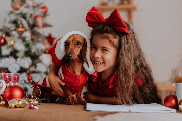 Una bambina carina e un bassotto nano in costume da Babbo Natale festeggiano il Natale e il Capodanno