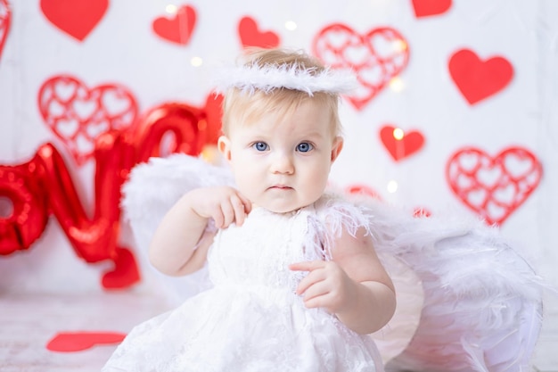 Una bambina carina in un costume da angelo con le ali su uno sfondo di cuori rossi e la scritta ama il concetto di san valentino il giorno di san valentino